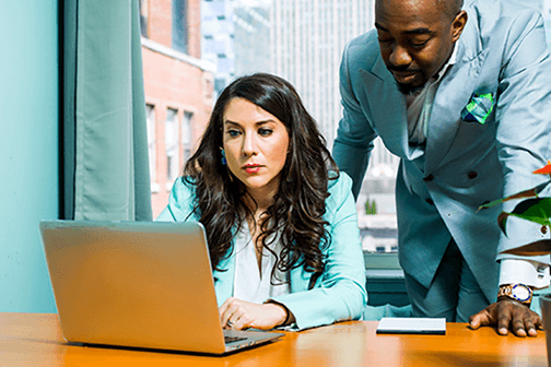 Two coworkers looking at a laptop while in an office.